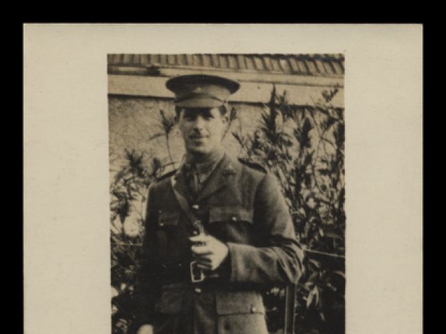 Photographic postcard of Keith McKeddie Doig in uniform holding a cane in his right hand, photographed full-length and outdoors 